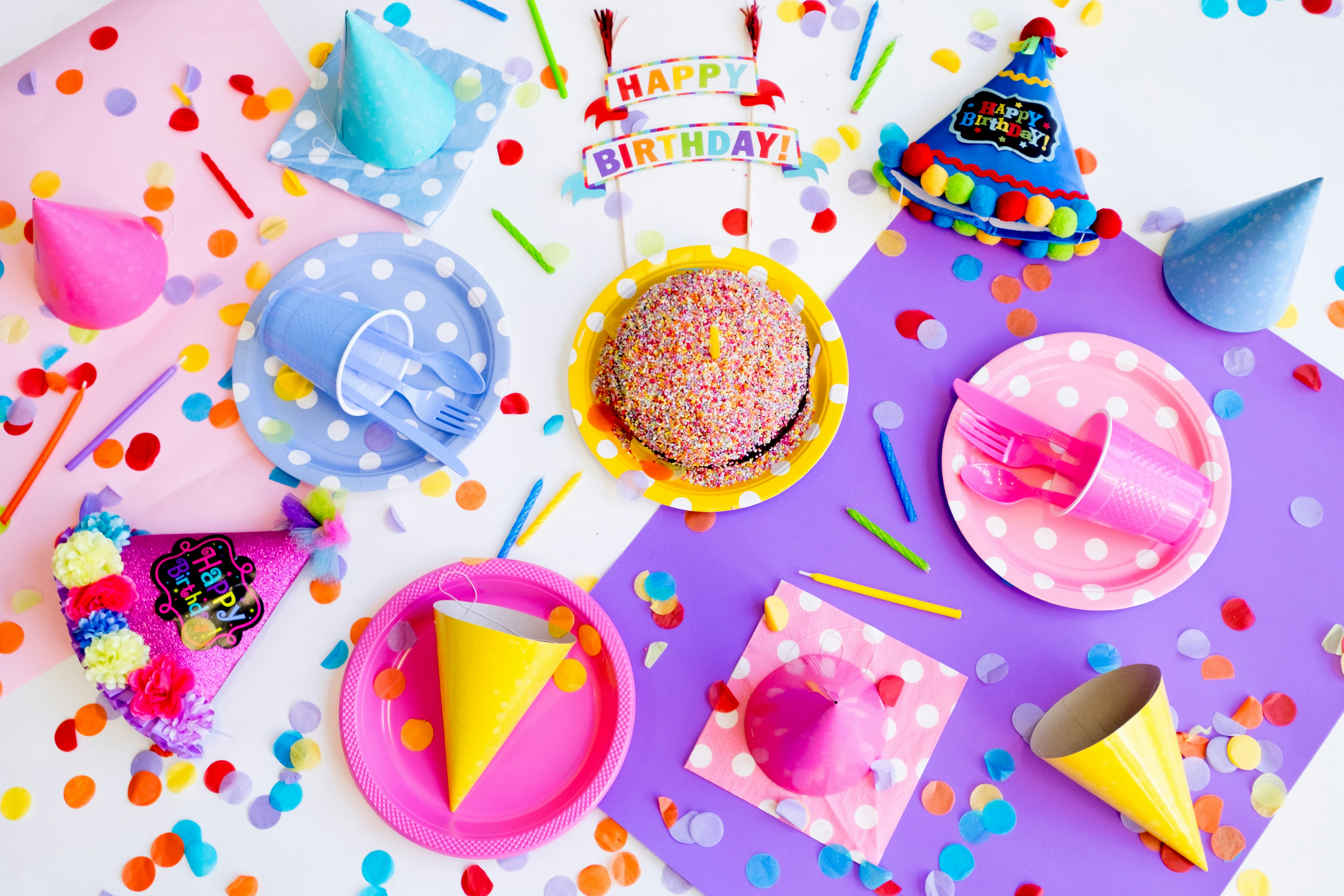 imagem com chapéu de festa, hambúrguer, pratos, confetes e frase happy birthday em uma superfície plana